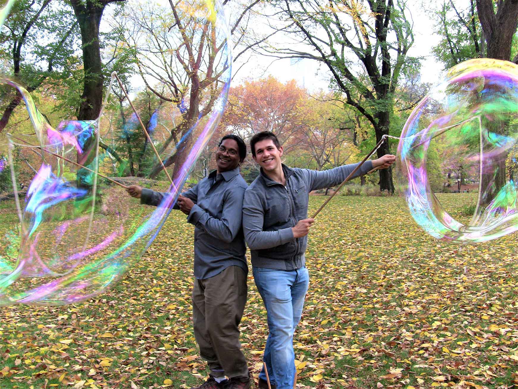 Two people making giant bubbles in an outdoor setting.