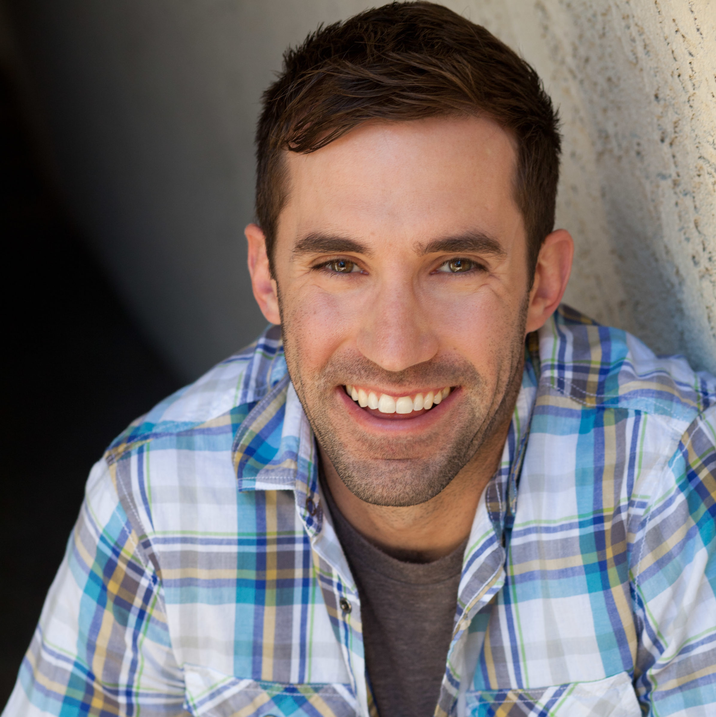 Michael Palascak is smiling while wearing a plaid button down with a gray t-shirt underneath.