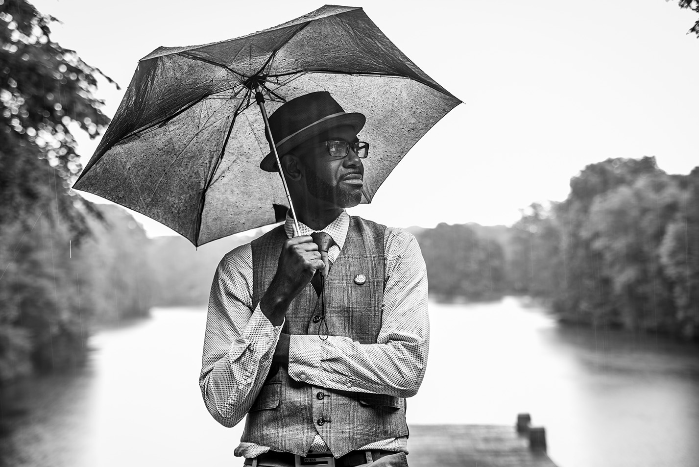 Poet Jon Goode is standing in front of a body of water while holding an umbrella.