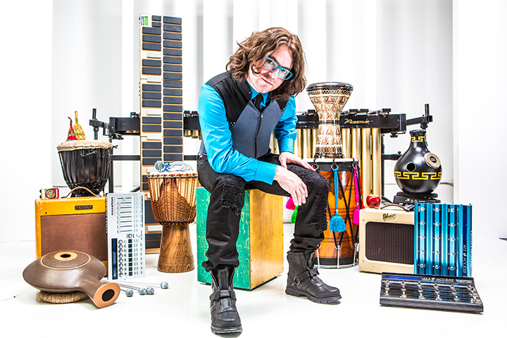 Noah Hoehn sitting on a box drum posing with all of his instruments.