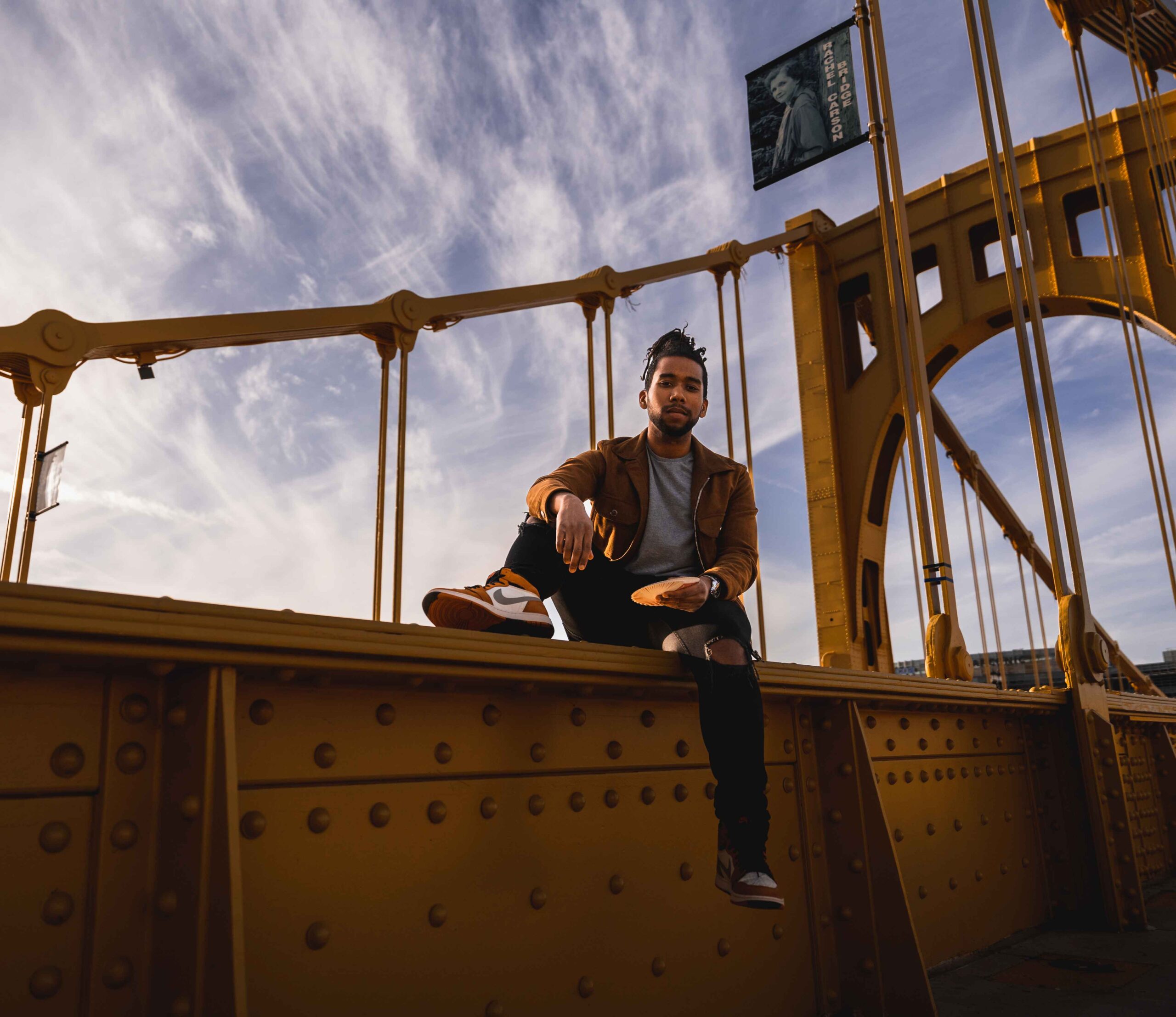 Noah Sonie sitting on the edge of a large yellow bridge.
