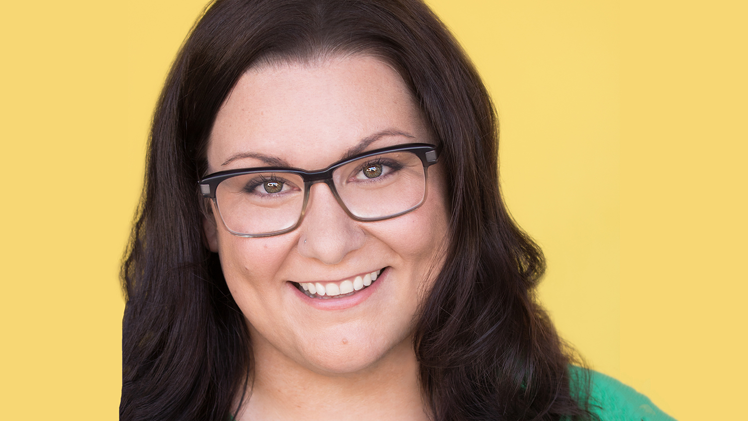 Jessi Campbell wearing glasses and smiling with a yellow background.
