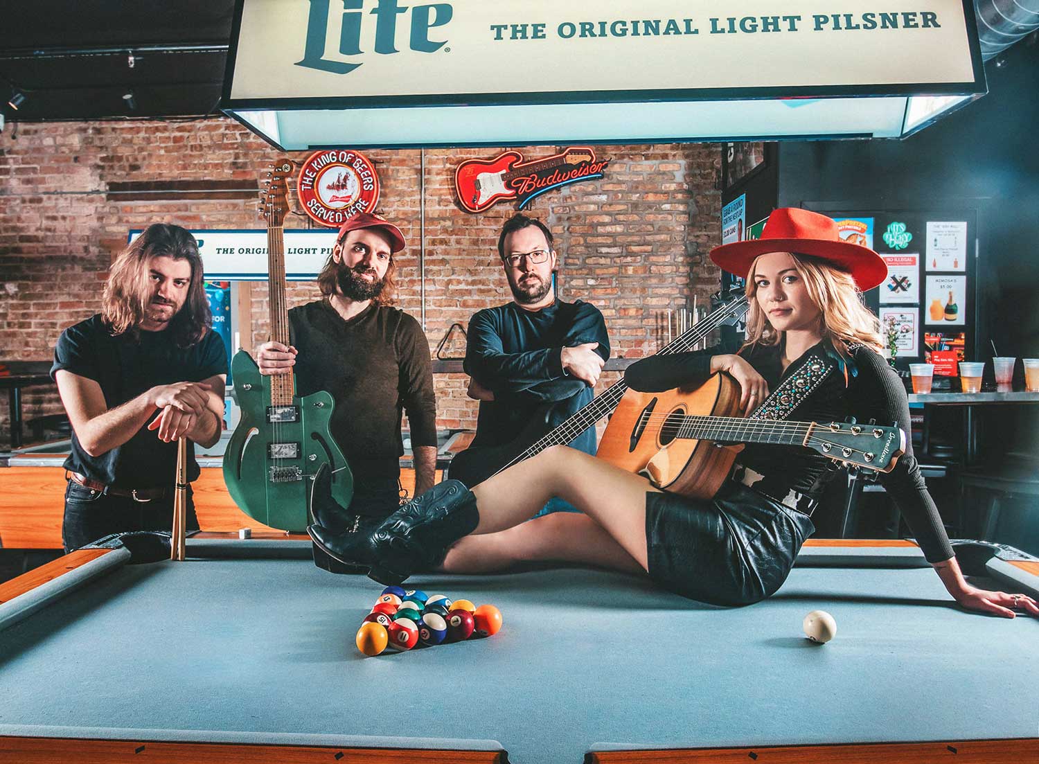 Mackenzie O'Brien sitting on a pool table with her band posing in the background.