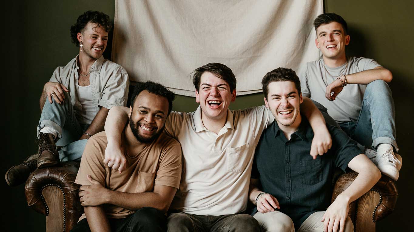 Members of Radius a cappella sitting on a couch and smiling while posing for a picture.